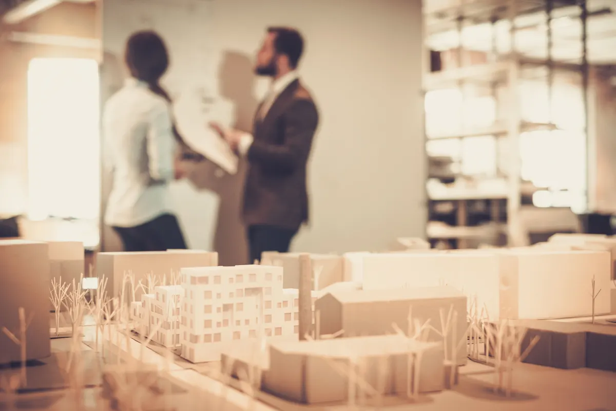 Architectural scale models with designers reviewing plans behind them