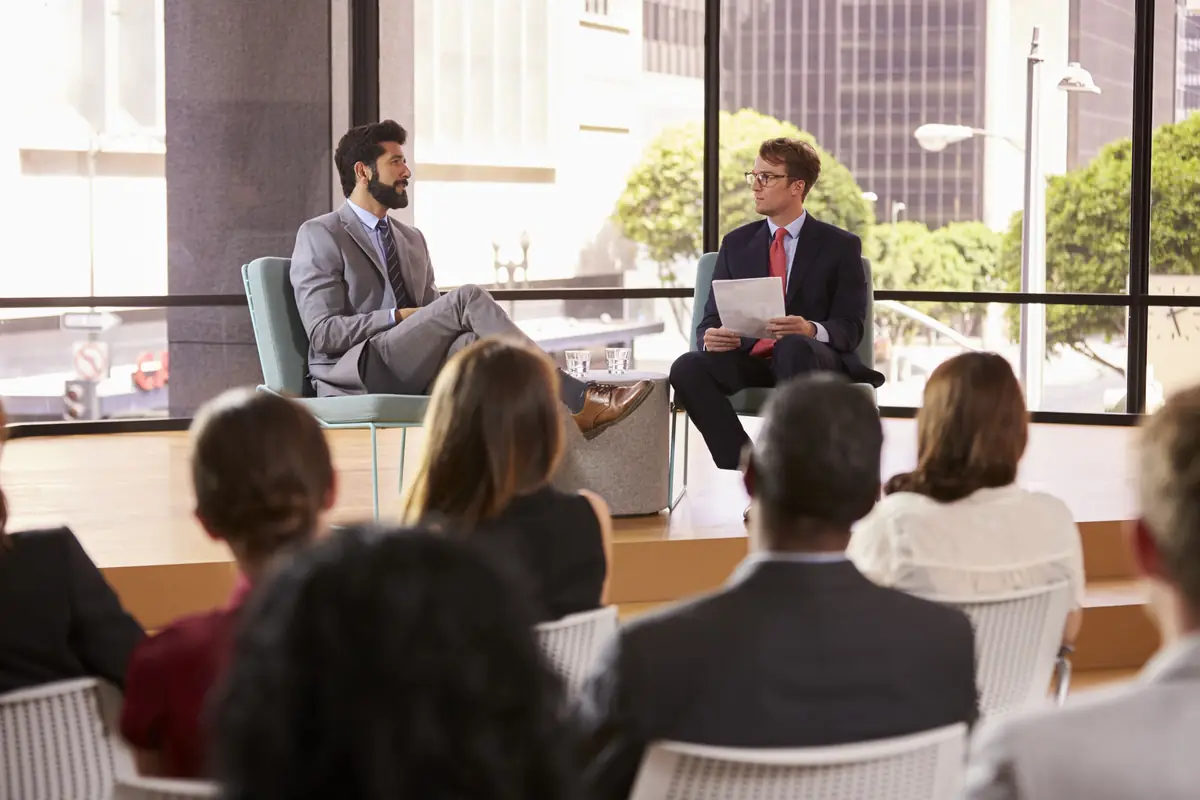 Speakers in a fireside conversation in front of a seated audience